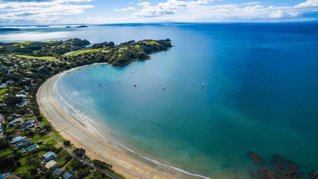 Beautiful aerial view of Oneroa Beach, Waiheke Island, featuring a sweeping sandy bay, turquoise waters, and anchored yachts. Discover New Zealand’s premier island destination for swimming, coastal walks, and relaxation.